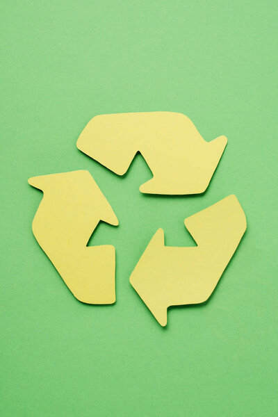 Вид сверху на желтый знак вторичной переработки со стрелками на зеленом фоне
