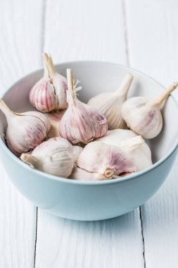 Beyaz ahşap masa üzerinde sarımsak ampuller ile mavi seramik kase