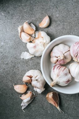 Top view of garlic in ceramic bowl and several peeled bulbs on grey background clipart