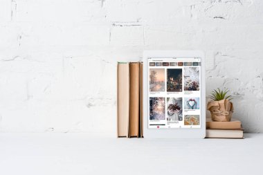 pinterest uygulama, kitap ve yakınındaki beyaz tuğla duvar Saksı bitki ile dijital tablet 