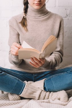 cropped shot of girl in knitted socks sitting and reading book clipart