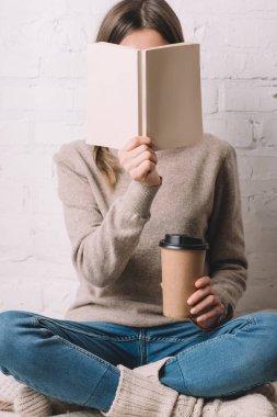 Kağıt bardak içinde gitmek için kitap ve kahve tutan kız