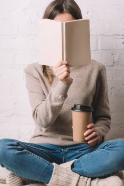 girl holding book and coffee to go in paper cup