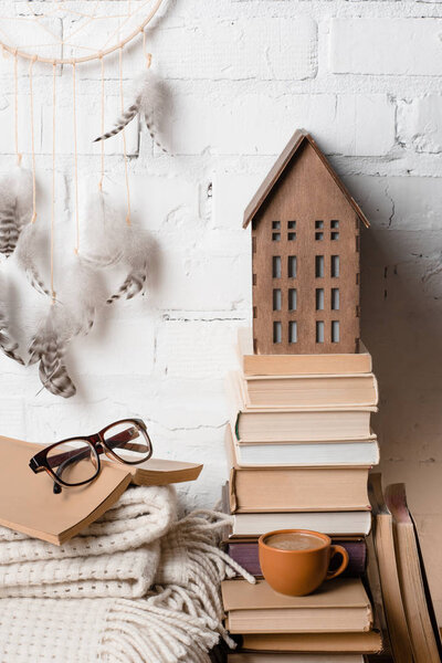 books, cup of coffee, eyeglasses, blanket and dream catcher near white brick wall