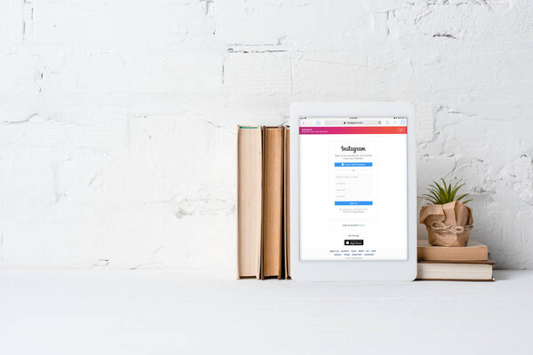 digital tablet with instagram application, books and potted plant near white brick wall