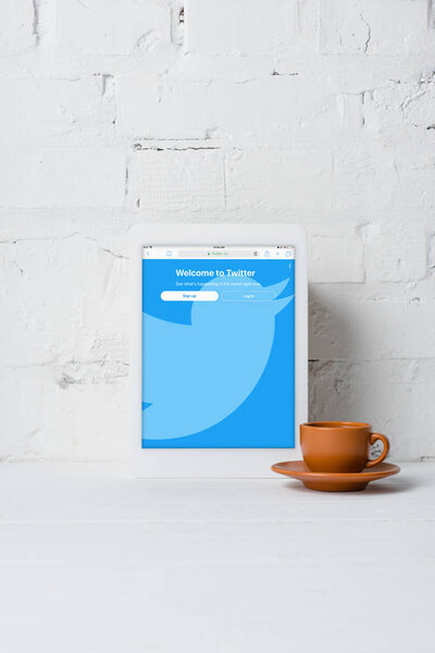 digital tablet with twitter application and cup of coffee near white brick wall 