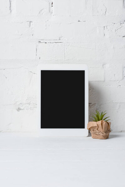 close-up view of digital tablet with blank screen and green potted plant near white brick wall