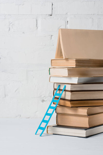 pile of books and small blue step ladder near white brick wall
