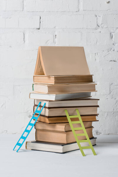 pile of books and small step ladders near white brick wall