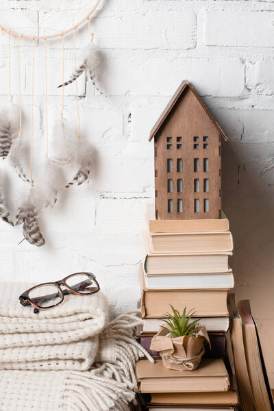 books, dream catcher, eyeglasses and decorative wooden house near white brick wall 