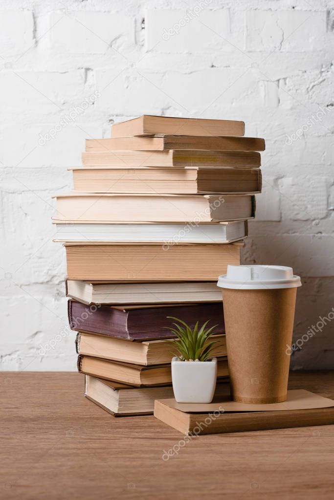 pile of books, green potted plant and coffee to go on wooden table