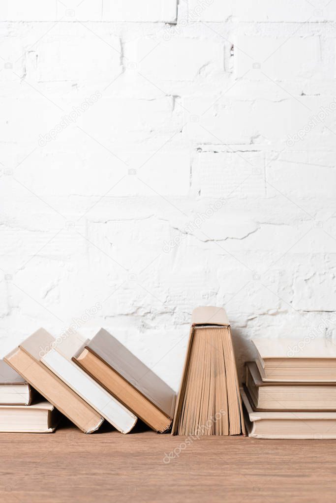 books with hardcovers on wooden table near white brick wall  