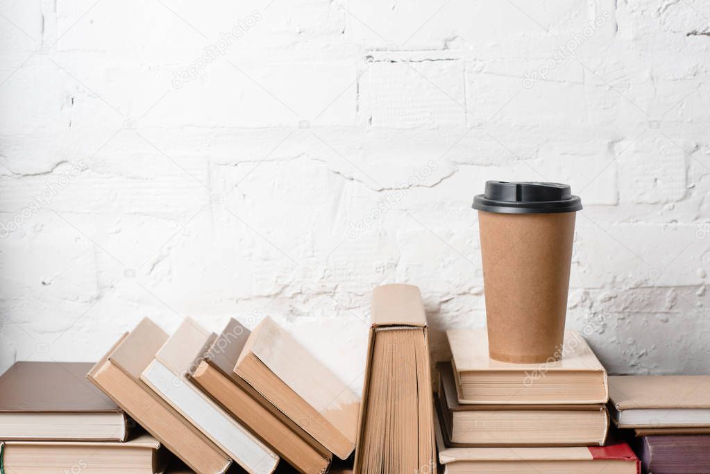 books with hardcovers and coffee to go near white brick wall 