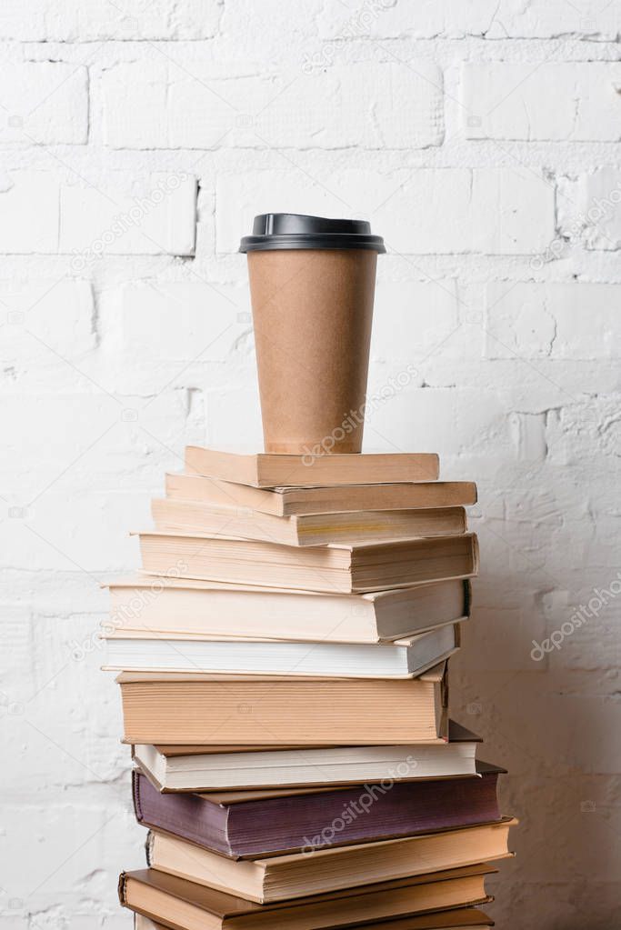 coffee to go on pile of books near white brick wall