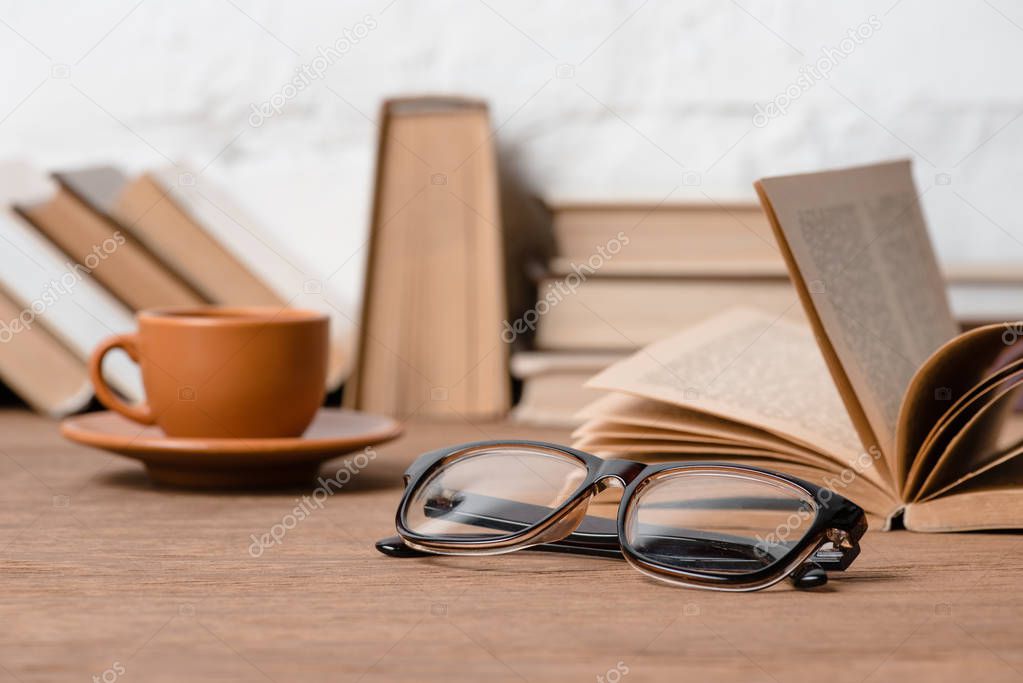 close-up view of eyeglasses, cup of coffee and books on wooden table