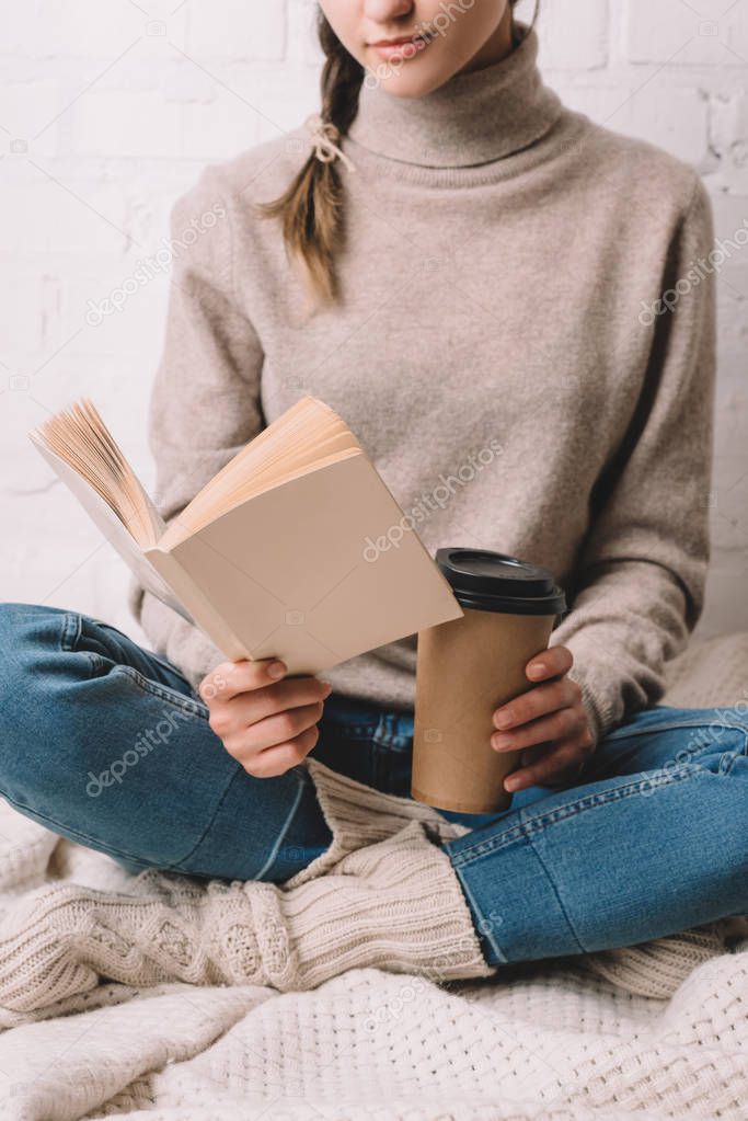 cropped shot of girl holding paper cup and reading book