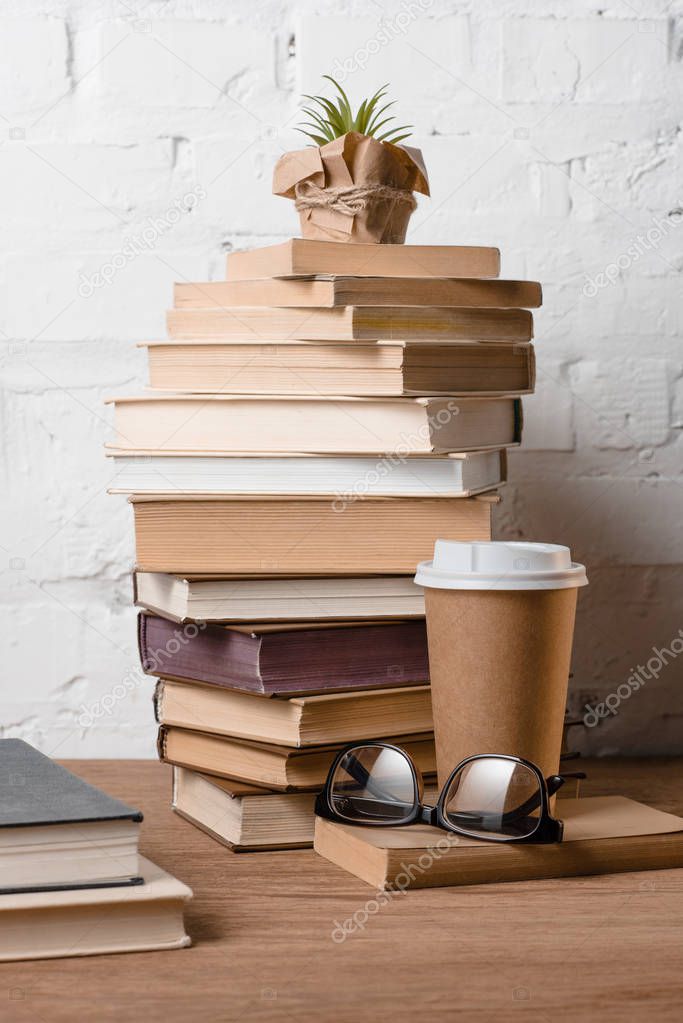 books, eyeglasses, potted plant and coffee to go on wooden table