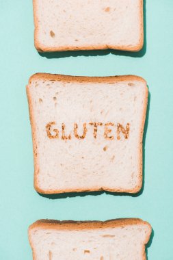 top view of row of bread slices with gluten sign on blue surface clipart