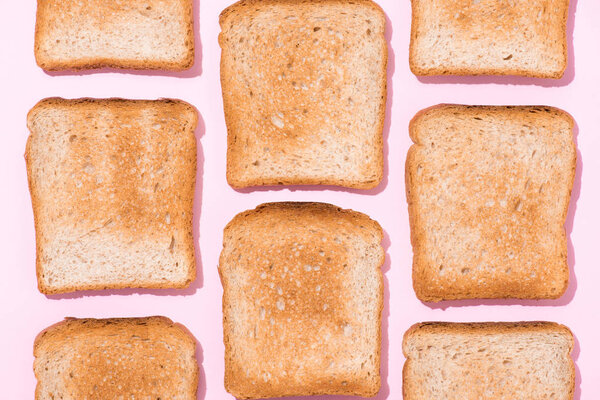 top view of repetitive pattern of crispy toasts on pink surface