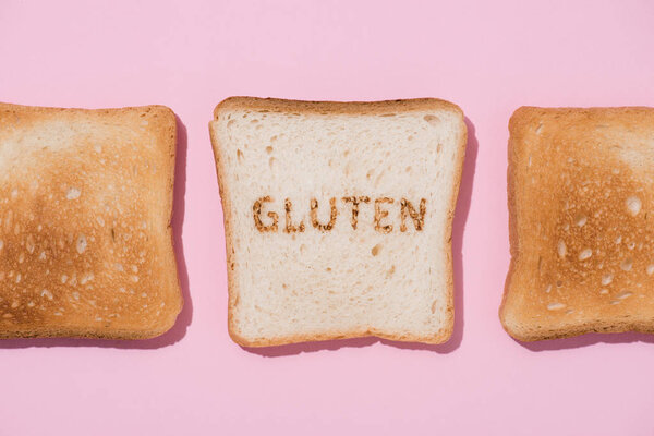 top view of row of toasts and slice of bread with burned gluten sign on pink surface
