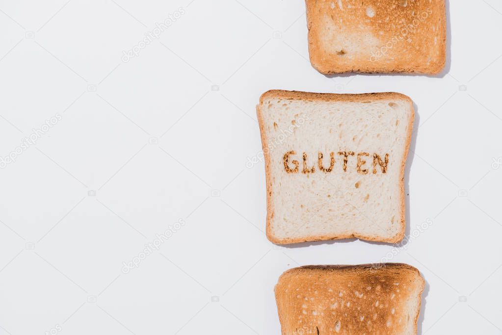top view of row of toasts and slice of bread with burned gluten sign on white surface