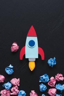cardboard rocket with pink and blue crumpled paper balls on black background, setting goals concept clipart