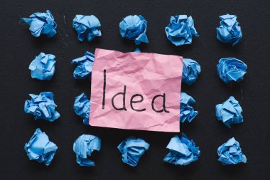 top view of 'idea' word written on sticky note with blue crumpled paper balls on black background, ideas concept clipart
