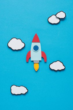 top view of paper rocket with clouds on blue background, setting goals concept clipart