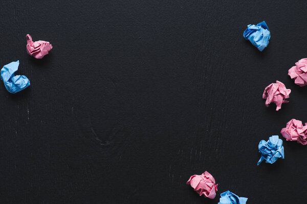 top view of scattered pink and blue crumpled paper balls on black background, think different concept