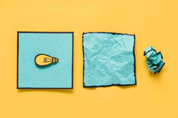 top view of note with light bulb drawing and crumpled paper on yellow background, ideas concept