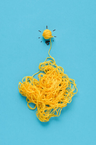 top view of light bulb sign made of yellow yarn on blue background, ideas concept