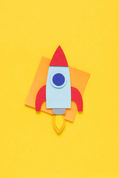 top view of flying paper rocket on yellow background, setting goals concept