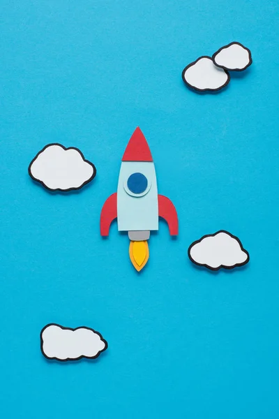 top view of paper rocket with clouds on blue background, setting goals concept