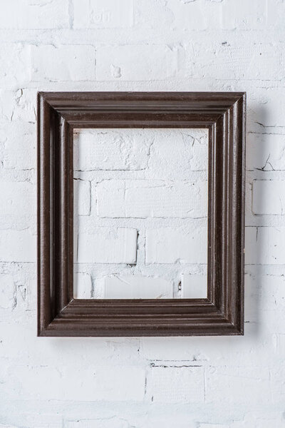 черная пустая рамка висит на белой кирпичной стене
