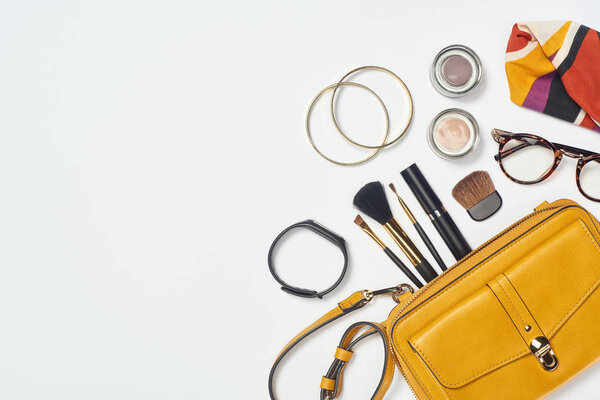 Top view of bracelets, scarf, glasses, mascara, cosmetic brushes, eyeshadow and bag on white background