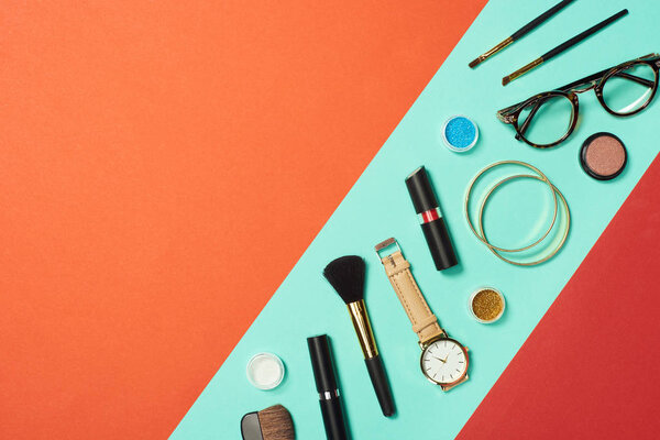 Mascara, watch, lipstick, bracelets, eyeshadow, blush, glasses and cosmetic brushes on turquoise background