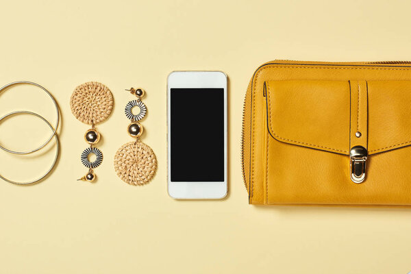 Top view of bracelets, earrings, smartphone and bag on yellow background