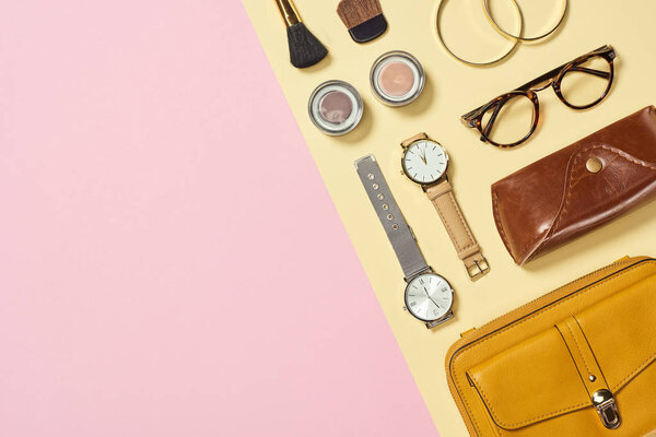 Top view of watches, yellow bag, case, glasses, eyeshadow, bracelets and cosmetic brushes