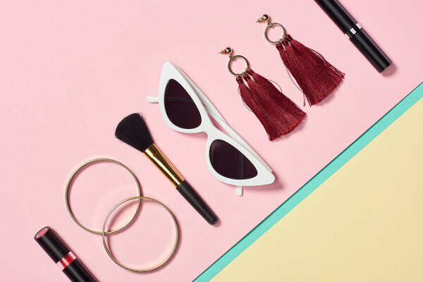 Flat lay with lipstick, bracelets, earrings, cosmetic brush, sunglasses and mascara