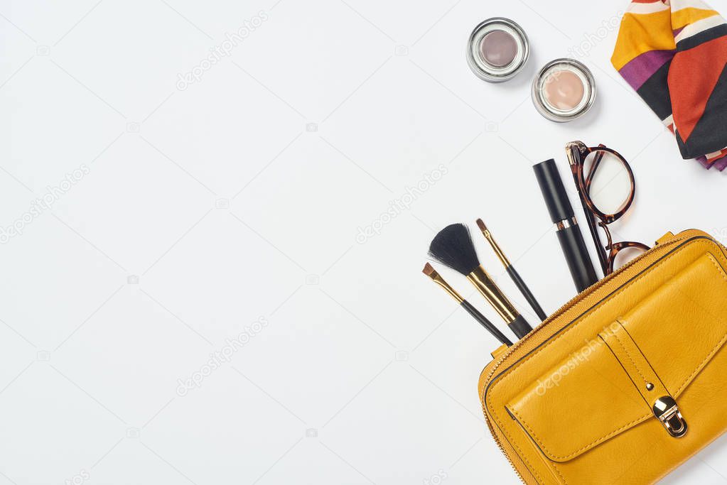 Top view of scarf, glasses, mascara, cosmetic brushes, eyeshadow and bag on white background