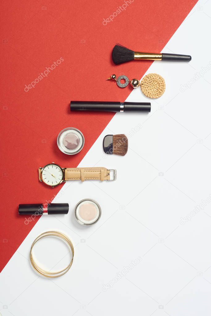Flat lay with mascara, watch, bracelets, eyeshadow, lipstick, earring and cosmetic brushes