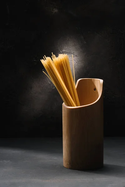 Bunch of uncooked spaghetti in wooden container with garlic on black surface — Stock Photo