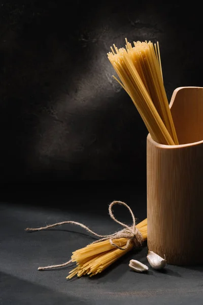 Raw spaghetti with garlic on black surface — Stock Photo