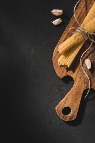 Vista superior de espaguetis atados con ajo sobre tabla de cortar de madera - foto de stock