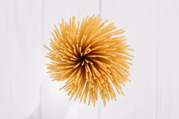 Vista dall'alto di un mazzo di spaghetti crudi su una superficie di legno bianca — Foto stock