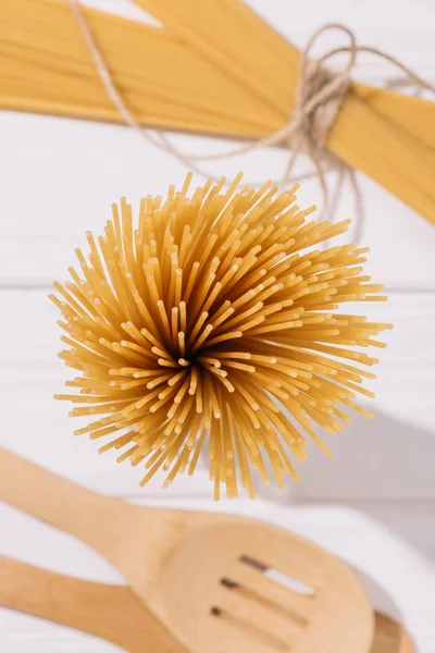 Draufsicht auf ein Bündel roher Spaghetti auf einer weißen Holzplatte mit Geschirr — Stockfoto