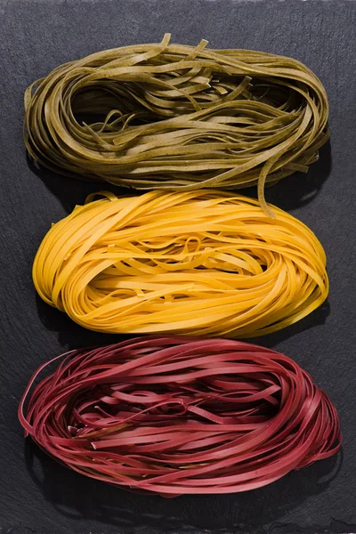 Vue de dessus de divers nids de spaghettis colorés sur noir — Photo de stock