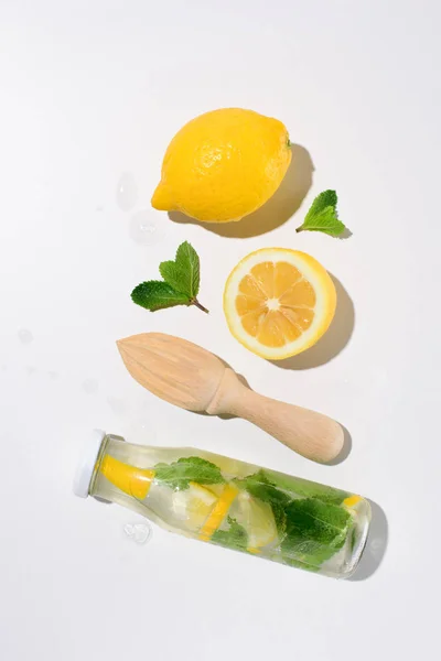 Vista superior de limones, hojas de menta, exprimidor de madera y botella de limonada - foto de stock