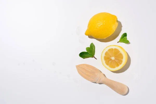 Top view of mint leaves, lemons and wooden squeezer on white surface — Stock Photo