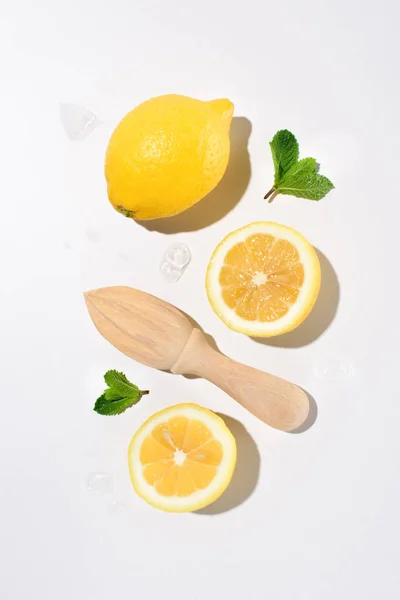 Elevated view of mint leaves, lemons and wooden squeezer on white surface — Stock Photo